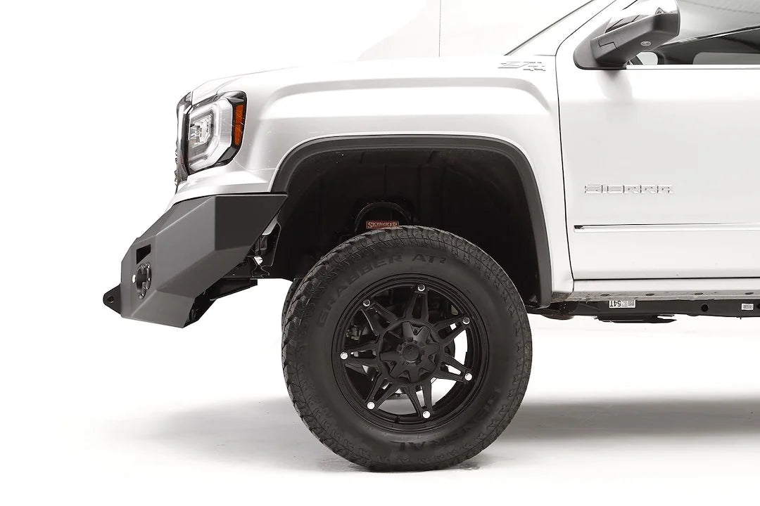 Fab Fours Premium Winch front bumper on a white GMC Sierra 1500, close-up of the front corner, showing the tapered end cap and wheel clearance
