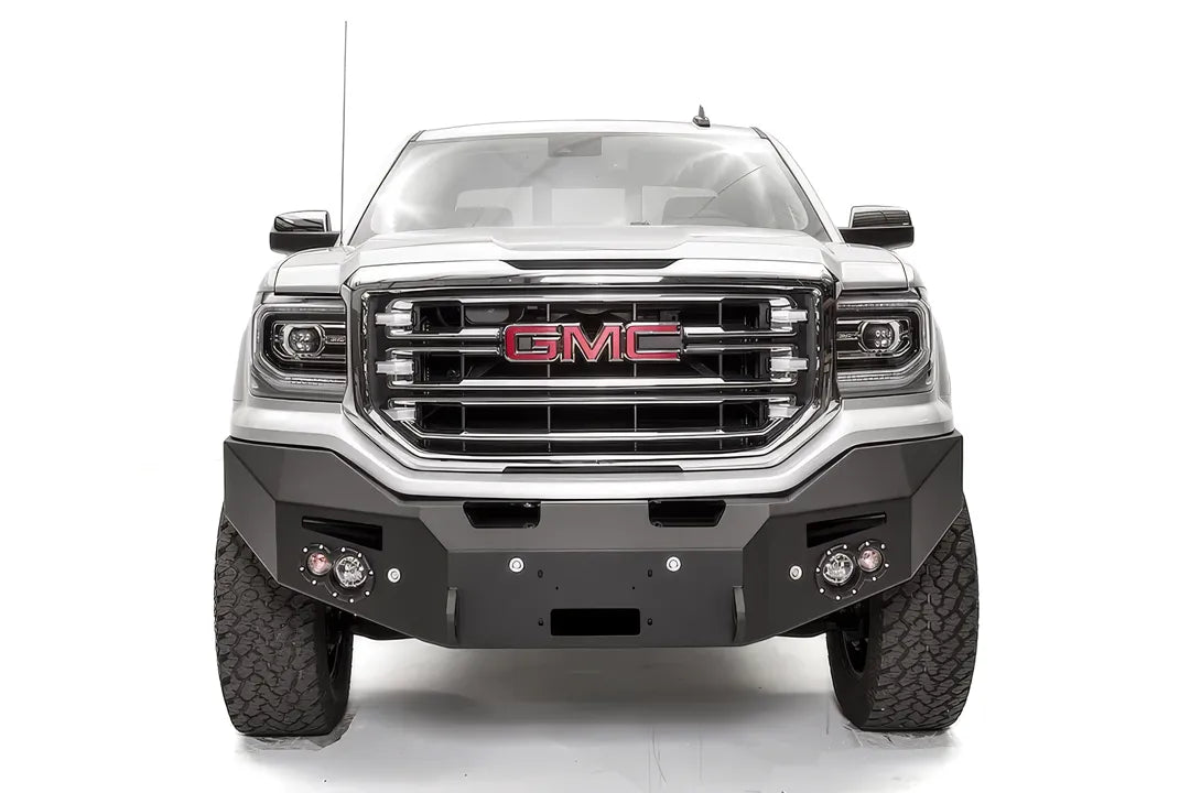 Fab Fours Premium Winch front bumper on a white GMC Sierra 1500, straight-on front view, showing the smooth plate bumper face, winch fairlead opening and round fog lights