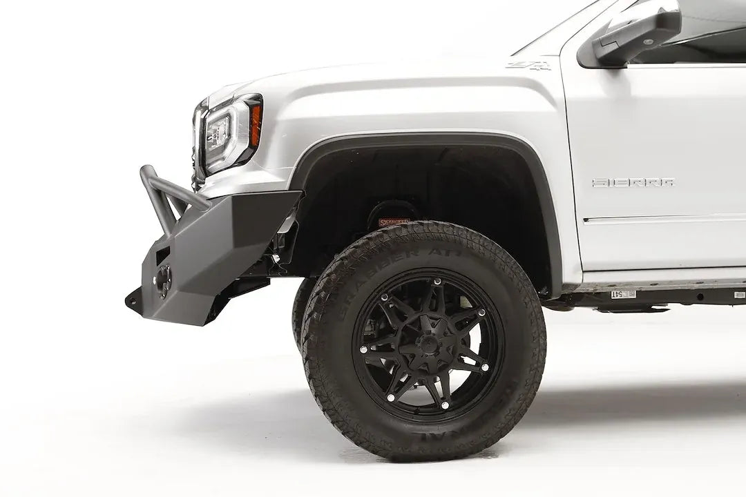 Fab Fours Premium Winch front bumper with pre-runner guard on a white GMC Sierra 1500, close-up of the front corner, showing the pre-runner tube, tapered end cap and wheel clearance