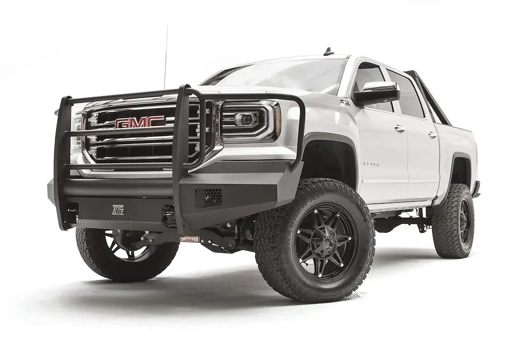Fab Fours Black Steel Elite front bumper with full guard on a white GMC Sierra 1500, driver-side front three-quarter view, showing the full grille guard with headlight hoops, smooth plate bumper face and mesh vent openings
