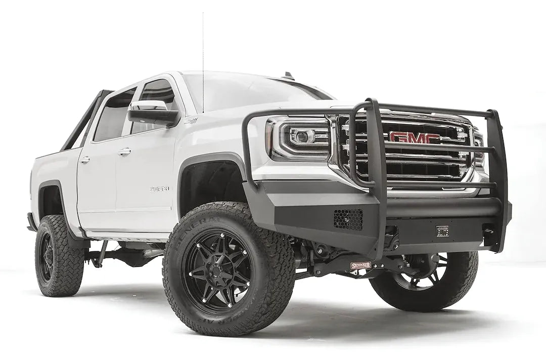 Fab Fours Black Steel Elite front bumper with full guard on a white GMC Sierra 1500, passenger-side front three-quarter view, showing the full grille guard with headlight hoops, smooth plate bumper face and mesh vent openings