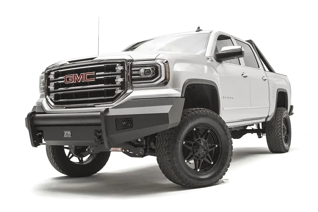 Fab Fours Black Steel Elite front bumper on a white GMC Sierra 1500, driver-side front three-quarter view, showing the smooth plate bumper face, mesh vent openings and light cutouts