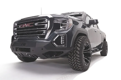 Fab Fours Vengeance front bumper on a dark gray GMC Sierra 1500, driver-side front three-quarter view, showing the angular bumper face, lower skid plate and wrapped end caps
