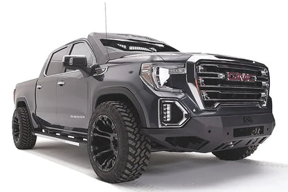 Fab Fours Vengeance front bumper on a dark gray GMC Sierra 1500, passenger-side front three-quarter view, showing the angular bumper face, light bar opening and wrapped end caps