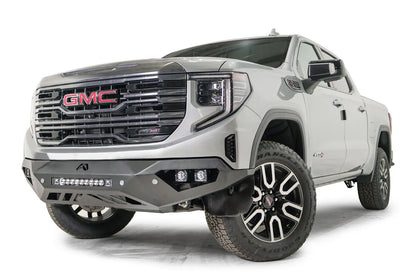 Fab Fours Vengeance front bumper on a silver GMC Sierra 1500, driver-side front three-quarter view, showing the angular bumper face, pod light cutouts and lower skid plate