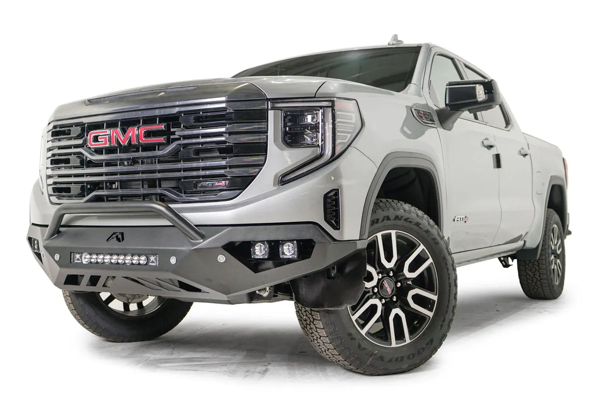 Fab Fours Vengeance front bumper with pre-runner guard on a silver GMC Sierra 1500, driver-side front three-quarter view, showing the low pre-runner bar, pod light cutouts and center light bar