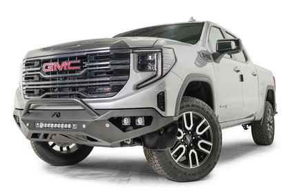 Fab Fours Vengeance front bumper with pre-runner guard on a silver GMC Sierra 1500, driver-side front three-quarter view, showing the low pre-runner bar, pod light cutouts and center light bar