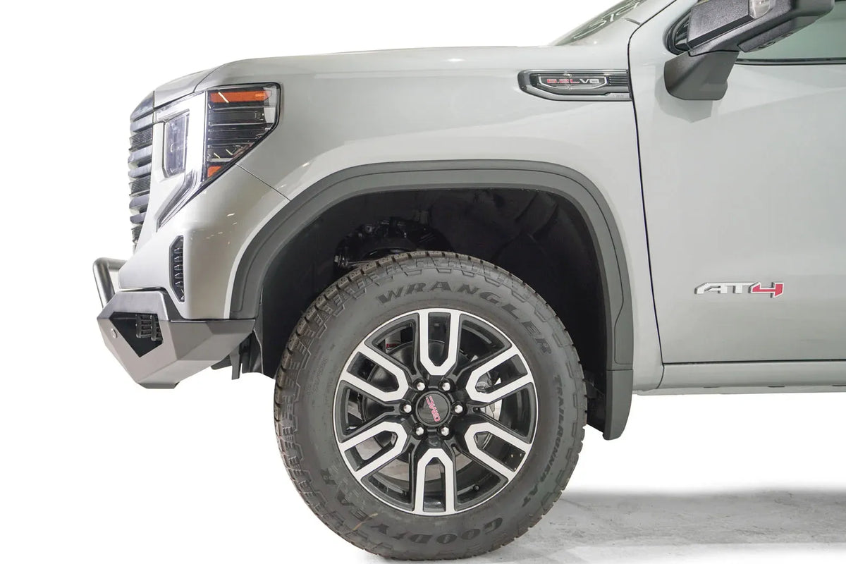 Fab Fours Vengeance front bumper with pre-runner guard on a silver GMC Sierra 1500, close-up of the driver-side front corner, showing the pre-runner bar end, bumper end cap and wheel clearance