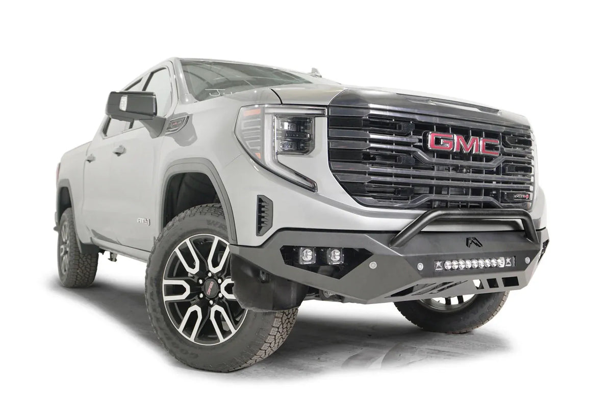 Fab Fours Vengeance front bumper with pre-runner guard on a silver GMC Sierra 1500, passenger-side front three-quarter view, showing the low pre-runner bar, pod light cutouts and lower skid plate