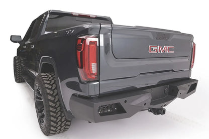Fab Fours Vengeance rear bumper with honeycomb mesh light openings on a dark gray GMC Sierra 1500, driver-side rear three-quarter view, with hitch receiver