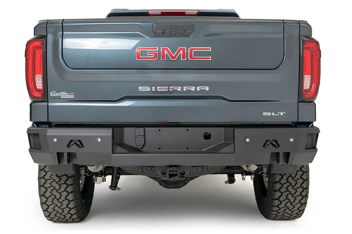 Fab Fours Premium Rear Bumper on a gray GMC Sierra 1500 SLT, rear view showing the matte black bumper with recessed license plate pocket, Fab Fours logo cutouts, sensor holes and retained receiver hitch