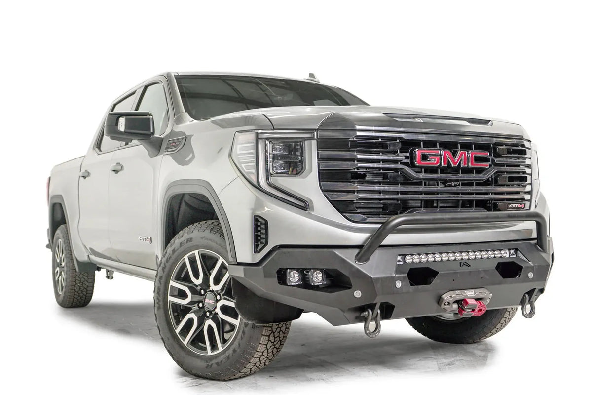 Fab Fours Matrix front bumper with pre-runner guard on a silver GMC Sierra 1500, passenger-side front three-quarter view, showing the pre-runner bar, light bar opening and D-ring shackle mounts