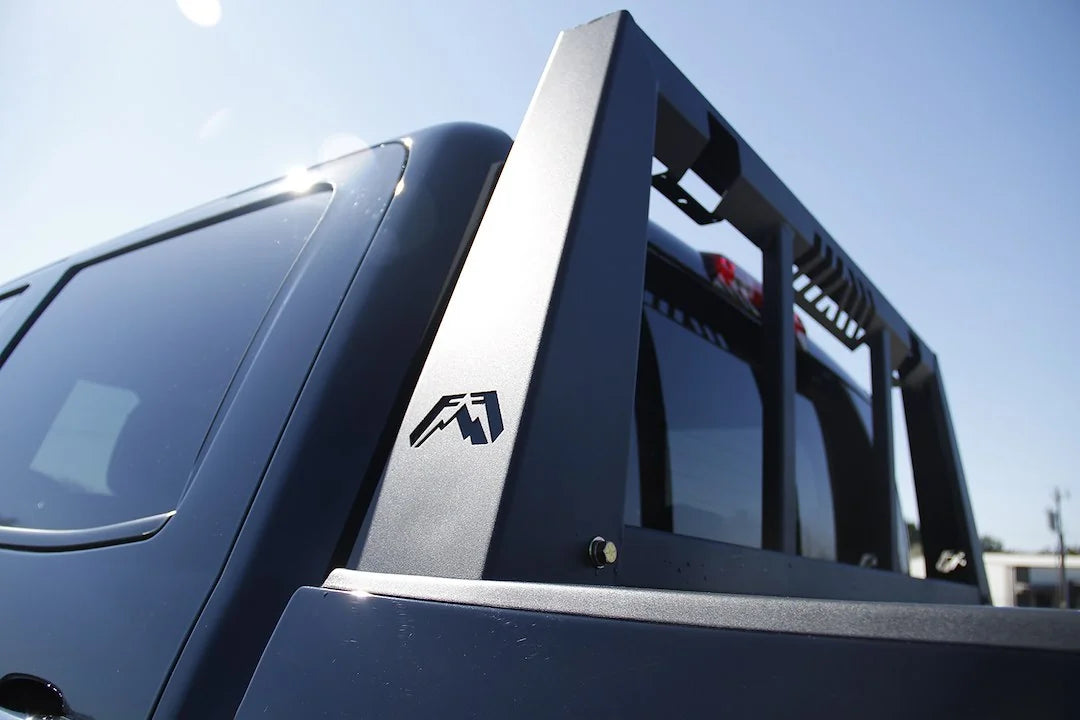 Fab Fours headache rack on a dark pickup, rear corner close-up outdoors, showing the tapered side post, Fab Fours logo cutout and window bars