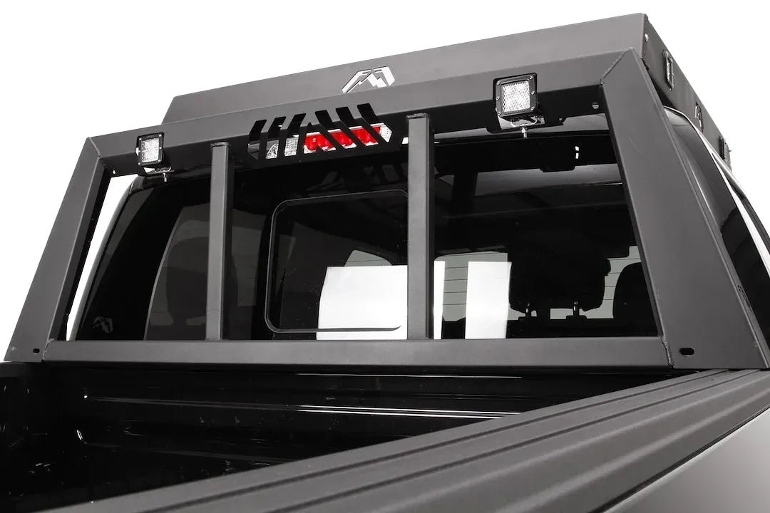 Fab Fours headache rack mounted behind the cab of a black Ford F-150, with two cube lights, a cutout for the third brake light, and Fab Fours logo, low angle view from the bed