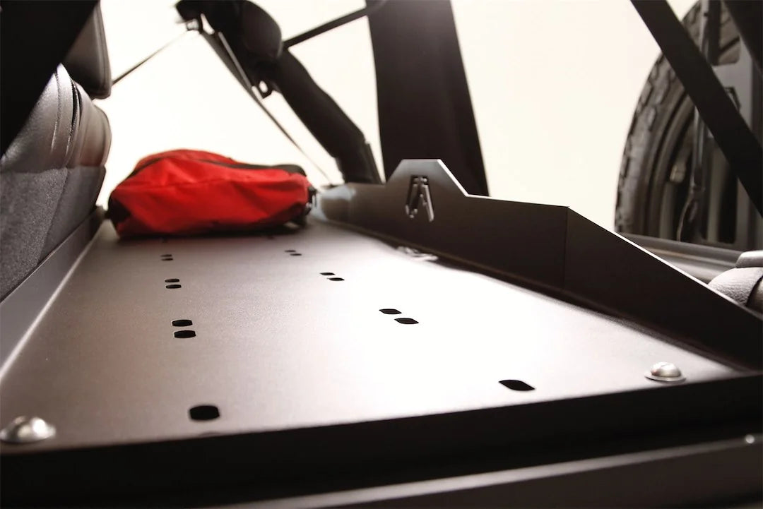 Close-up of the Fab Fours cargo divider shelf in a Jeep Wrangler JK, showing the slotted tie-down points and raised logo edge with a red bag on top