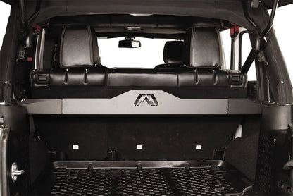 Fab Fours cargo divider installed behind the rear seat of a Jeep Wrangler JK, rear view through the open tailgate, showing the steel shelf with Fab Fours logo cutout