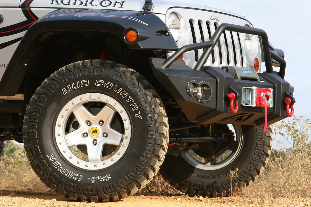 Fab Fours Lifestyle Winch bumper with pre-runner guard on a silver Jeep Wrangler JK, close-up of the front corner outdoors, showing the pre-runner hoop, winch and red D-ring shackles
