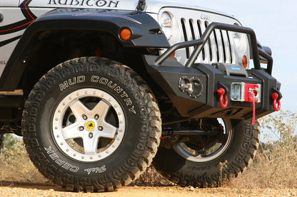 Fab Fours Lifestyle Winch bumper with pre-runner guard on a silver Jeep Wrangler JK, close-up of the front corner outdoors, showing the pre-runner hoop, winch and red D-ring shackles