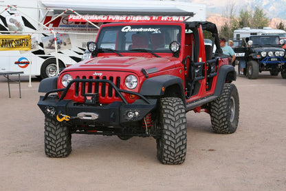 Fab Fours Lifestyle Winch bumper with pre-runner guard on a red Jeep Wrangler JK, front view outdoors, showing the pre-runner hoop, winch mount and round fog lights