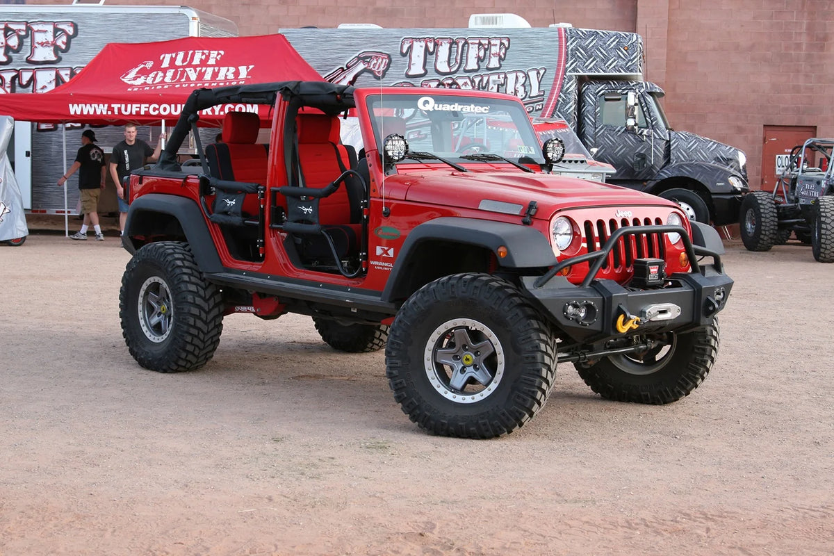 Fab Fours Lifestyle Winch bumper with pre-runner guard on a red Jeep Wrangler JK, passenger-side front three-quarter view outdoors, showing the pre-runner hoop, winch mount and round fog lights