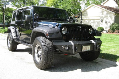 Fab Fours Lifestyle Winch bumper on a dark blue Jeep Wrangler JK Rubicon, passenger-side front three-quarter view outdoors, showing the bumper face, fog lights and end caps
