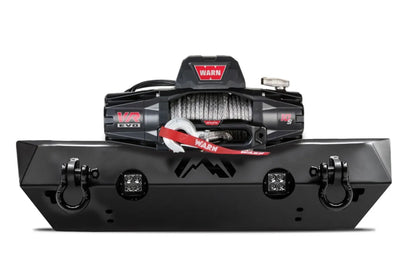 Fab Fours Hardcore Stubby Winch bumper in black powder coat, front view, showing the winch mount with winch installed, cube light cutouts and D-ring shackles