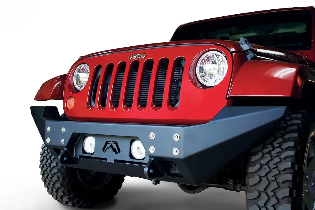 Fab Fours Full Metal Jacket full-width front bumper on a red Jeep Wrangler JK, front three-quarter close-up, showing the bolted face plate, round fog lights and full-width end caps