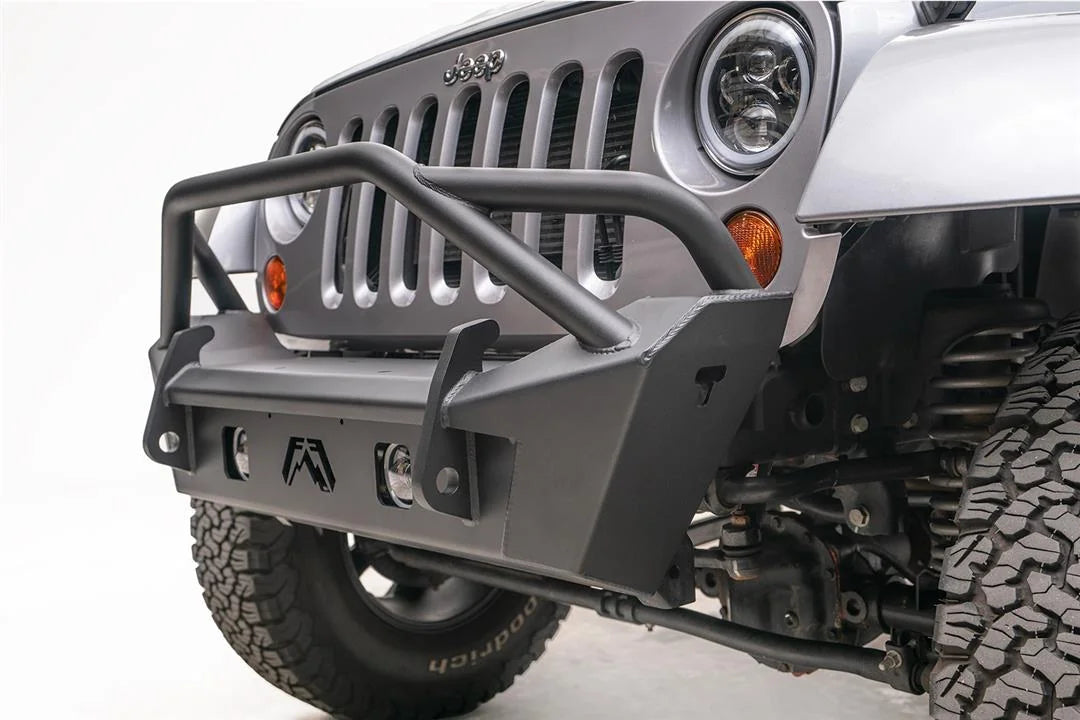 Fab Fours Stubby bumper with pre-runner guard on a silver Jeep Wrangler JK, close-up of the front corner, showing the pre-runner hoop, Fab Fours logo cutout and fog light opening