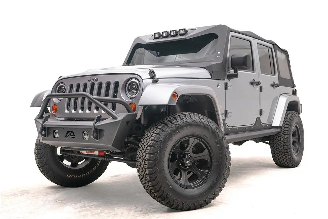 Fab Fours Stubby bumper with pre-runner guard on a silver Jeep Wrangler JK, driver-side front three-quarter view, showing the pre-runner hoop, stubby end caps and fog light openings