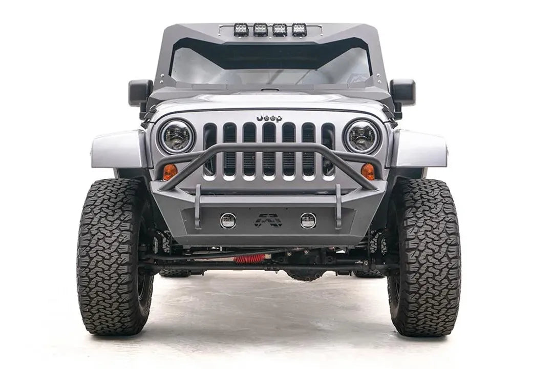 Fab Fours Stubby bumper with pre-runner guard on a silver Jeep Wrangler JK, straight-on front view, showing the pre-runner hoop, fog light openings and Fab Fours logo cutout
