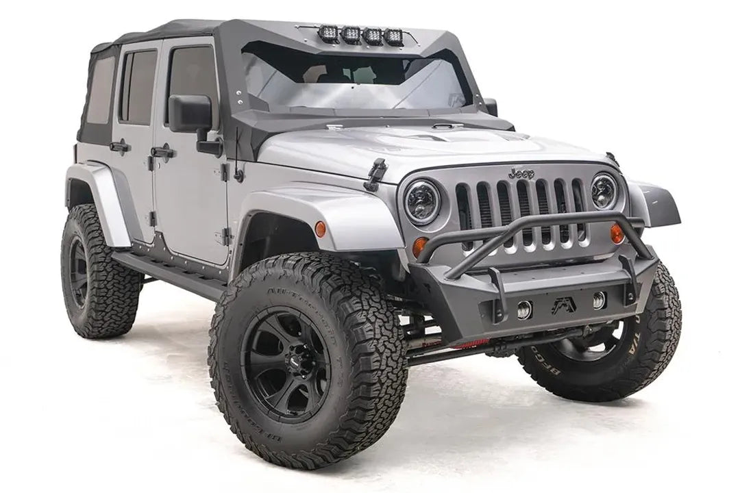 Fab Fours Stubby bumper with pre-runner guard on a silver Jeep Wrangler JK, passenger-side front three-quarter view, showing the pre-runner hoop, stubby end caps and fog light openings