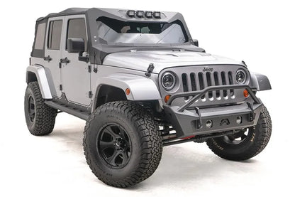 Fab Fours Stubby bumper with pre-runner guard on a silver Jeep Wrangler JK, passenger-side front three-quarter view, showing the pre-runner hoop, stubby end caps and fog light openings