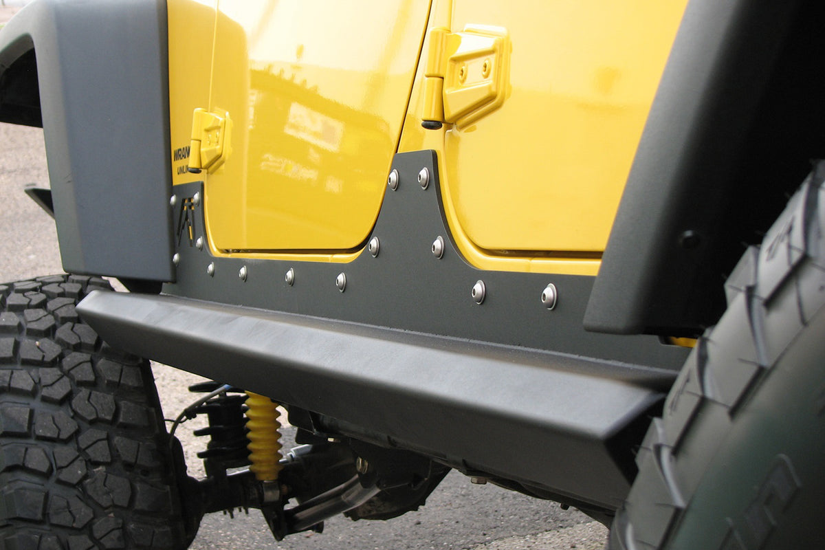 Fab Fours HardCore Rock Sliders on a yellow Jeep Wrangler JK, close-up outdoors, showing the tubular slider rail, riveted rocker plate and black powder coat finish