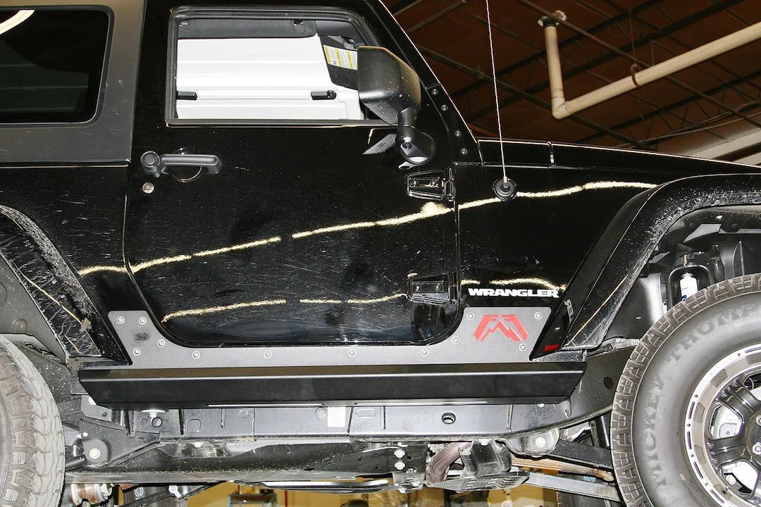 Fab Fours HardCore Rock Sliders on a black Jeep Wrangler JK, close-up of the rocker on a lift, showing the slider rail, riveted rocker plate and Fab Fours logo