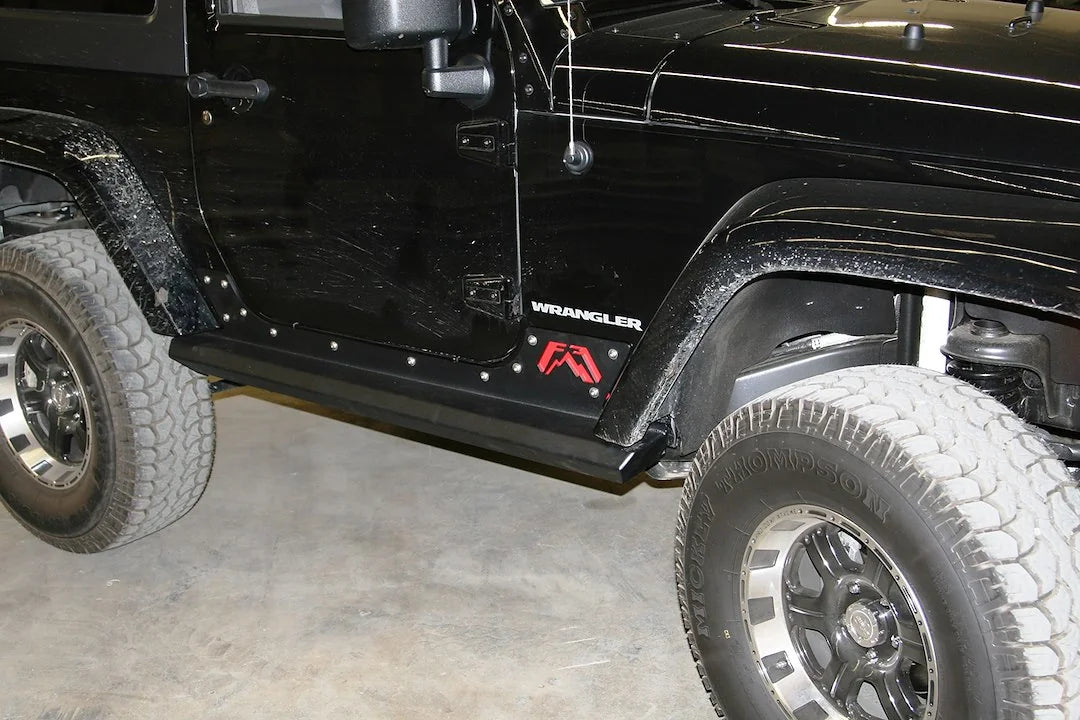 Fab Fours HardCore Rock Sliders on a black Jeep Wrangler JK, close-up of the rocker in a garage, showing the slider rail, riveted rocker plate and Fab Fours logo