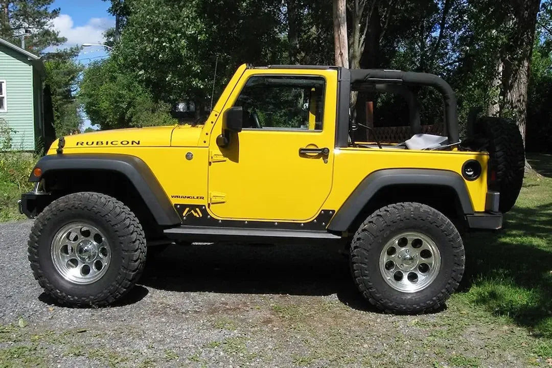 Fab Fours HardCore Rock Sliders on a yellow 2-door Jeep Wrangler JK Rubicon, driver-side profile view outdoors, showing the slider rail along the rocker and riveted rocker plate
