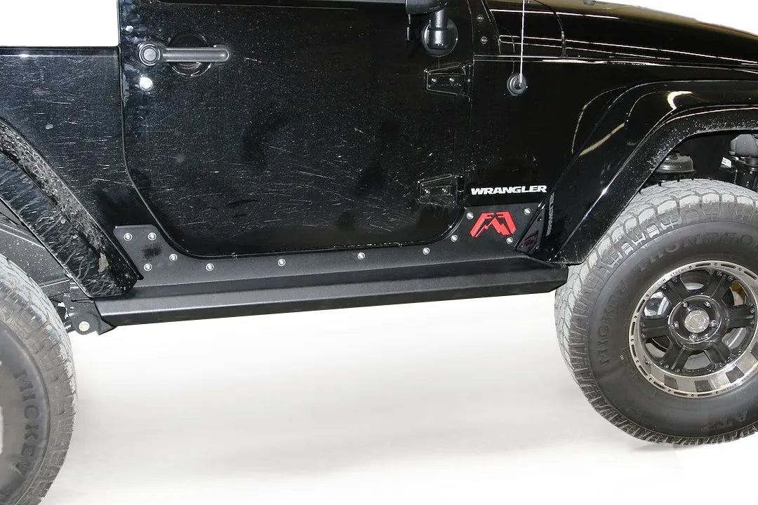Fab Fours HardCore Rock Sliders on a black Jeep Wrangler JK, close-up of the rocker in a garage, showing the slider rail, riveted rocker plate and Fab Fours logo