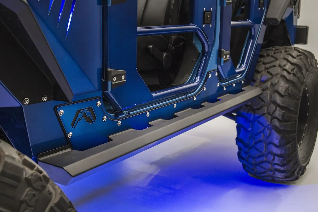 Fab Fours Light Rock Slider on a blue Jeep Wrangler JK, low driver-side view, showing the flat black rocker guard with notched step edge, Fab Fours logo plate and blue rock lights glowing underneath