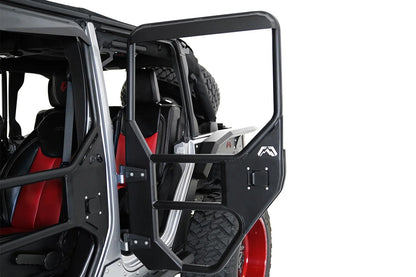 Fab Fours full tube door on a silver Jeep Wrangler JK Unlimited, driver-side rear door swung open, showing the black tubular frame with steel lower panel, paddle latch and Fab Fours logo, with the spare tire behind