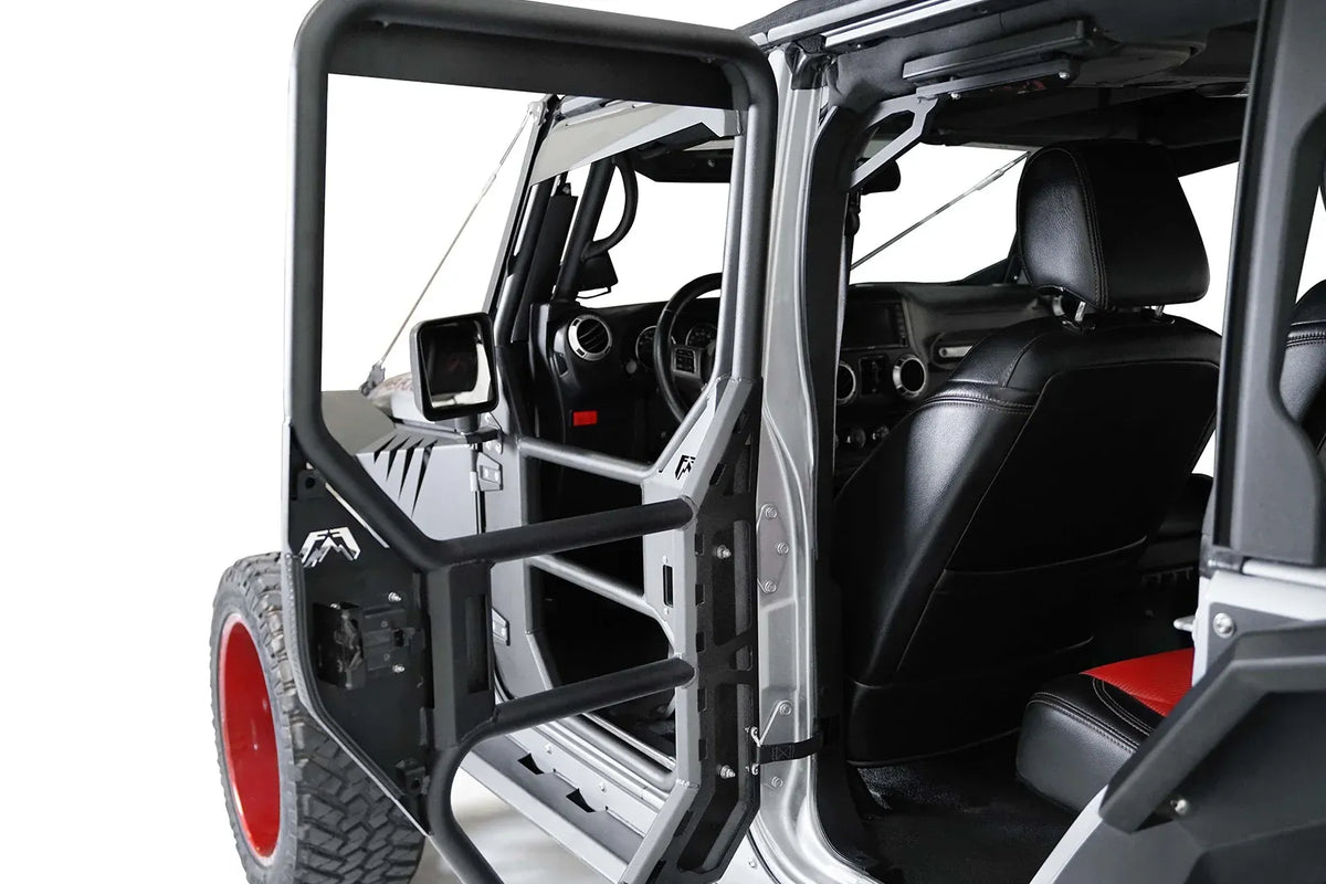 Fab Fours full tube door on a silver Jeep Wrangler JK, driver-side front door swung open, showing the black tubular frame with steel lower panel, Fab Fours logo, mirror mount and the factory hinge and check strap