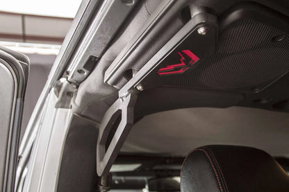 Fab Fours grab handle installed on the roll bar of a Jeep Wrangler JK, close-up showing the matte black steel handle with red Fab Fours logo bolted near the door opening