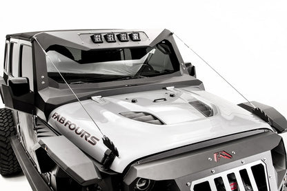 Fab Fours limb risers on a silver Jeep Wrangler, elevated front view, showing steel cables running from the jagged hood-mounted brackets to the corners of the Fab Fours windshield frame with pod lights