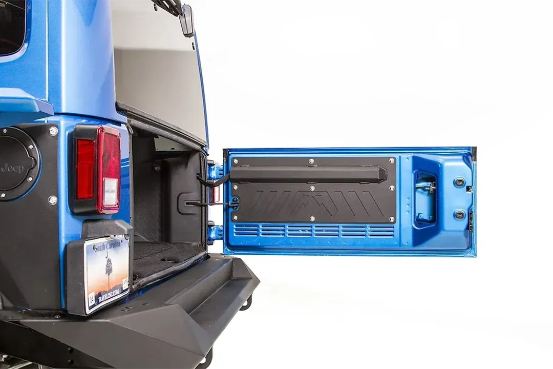 Fab Fours tailgate plate on a blue Jeep Wrangler JK, rear view with the tailgate swung open, showing the black plate with the Fab Fours logo bolted to the inside of the tailgate