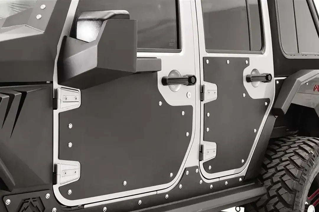 Fab Fours door skins on the front and rear doors of a Jeep Wrangler JK Unlimited, close-up from the driver side, showing the black riveted panels inside the silver door frames with the mirror mount on the front door