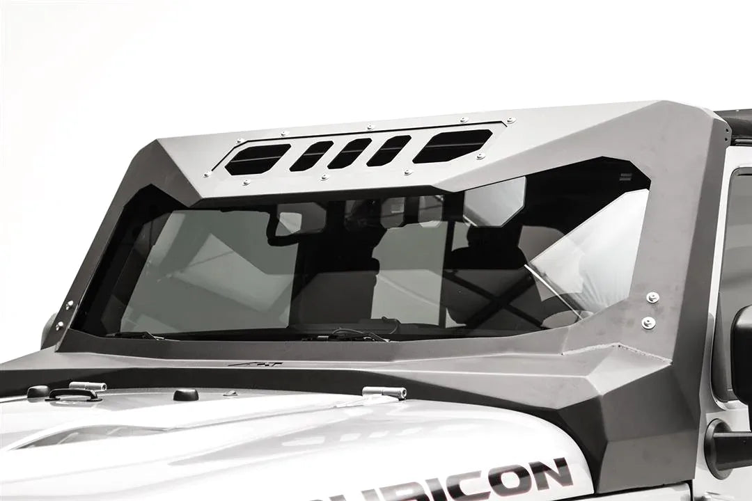 Close-up of the Fab Fours ViCowl on a silver Jeep Wrangler JK Rubicon, driver side, showing the formed steel A-pillar cover and slotted visor panel over the windshield
