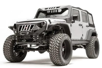 Fab Fours ViCowl on a lifted silver Jeep Wrangler JK Rubicon, front driver-side view, showing the steel windshield cowl with slotted roof visor plus matching Fab Fours grille guard, winch bumper and fender armor