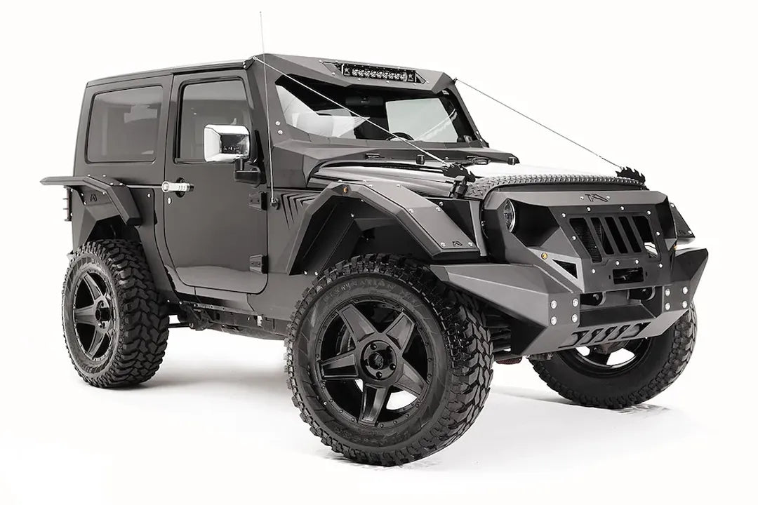 Fab Fours rear fender base on a dark gray 2-door Jeep Wrangler JK, passenger-side front three-quarter view, showing the riveted fender armor and wheel clearance