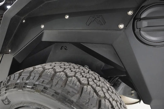 Fab Fours inner fender and fender flare in the driver-side rear wheel well of a black Jeep Wrangler JL, with Fab Fours logo cutouts