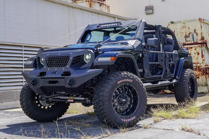 Fab Fours ViCowl Limb Riser on a lifted black Jeep Wrangler JL outdoors, front driver-side view, with stainless cables running from the hood to the ViCowl to deflect branches