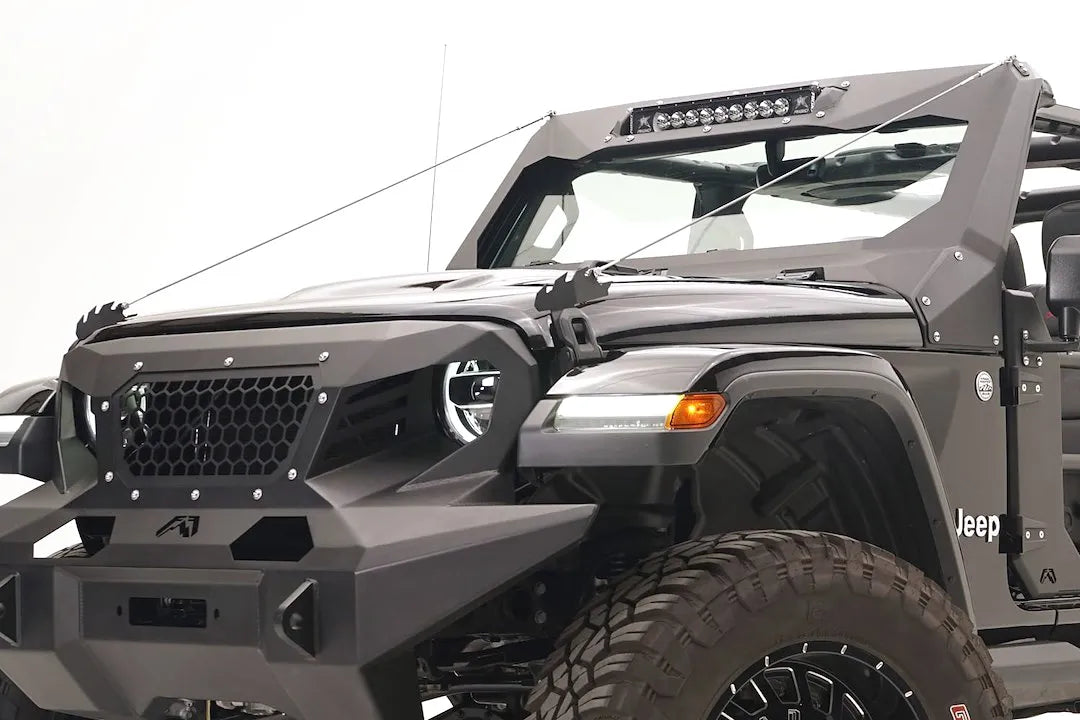 Fab Fours ViCowl Limb Riser on a black Jeep Wrangler JL, front driver-side view, showing both limb riser cables stretched from the hood brackets to the top of the ViCowl